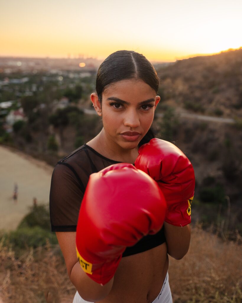A fierce, beautiful young woman in red boxing gloves on the top of a hillside.